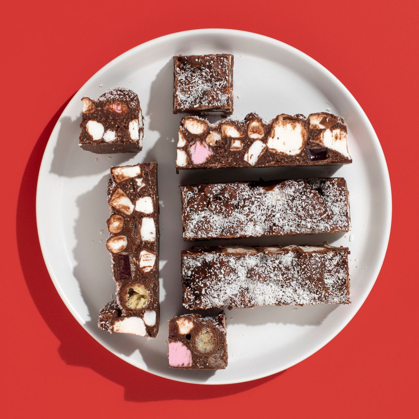 Assorted chocolate brownies on a white plate against a red background