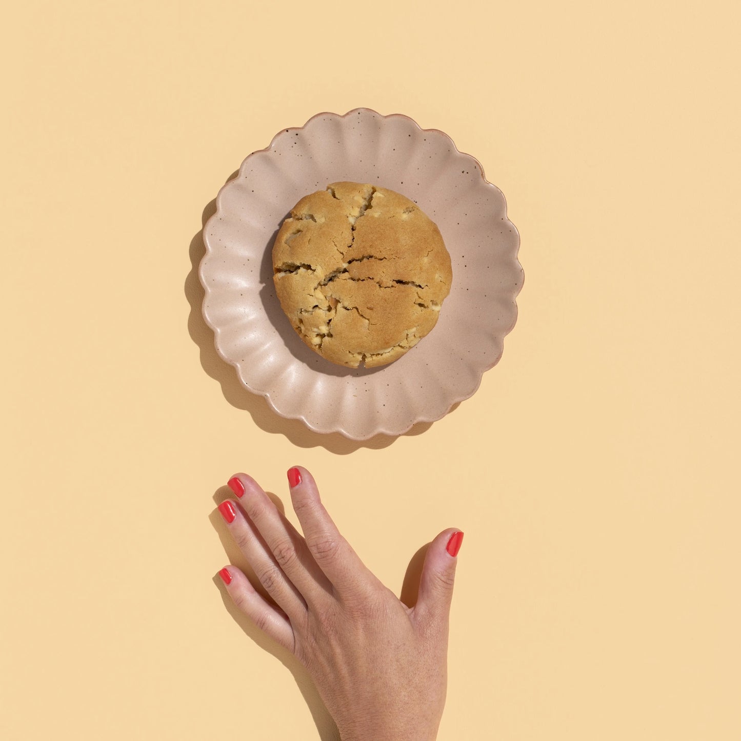 white choc macadamia loaded cookie. on a plate with hand reaching for it