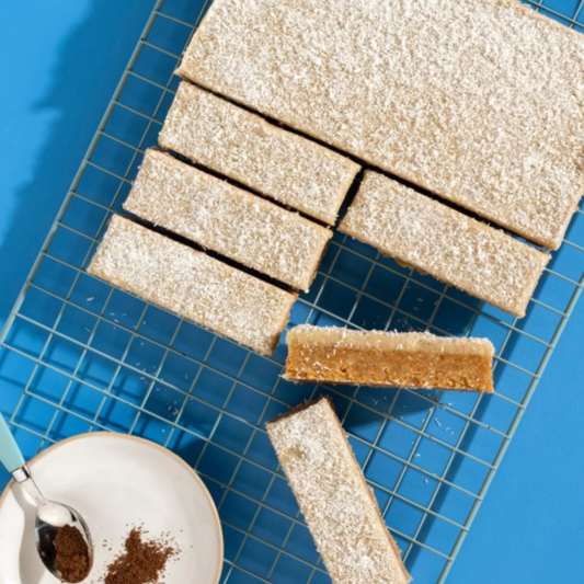 Sliced cake bars on a cooling rack with a cup of coffee and spoon on a blue tiled background