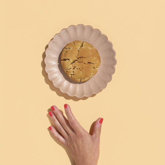 white choc macadamia loaded cookie. on a plate with hand reaching for it